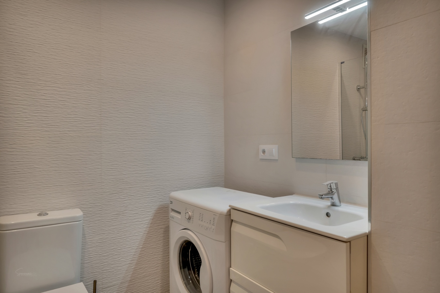 Detalle de baño con lavabo encastrado, lavadora y paredes texturizadas en tonos neutros.
