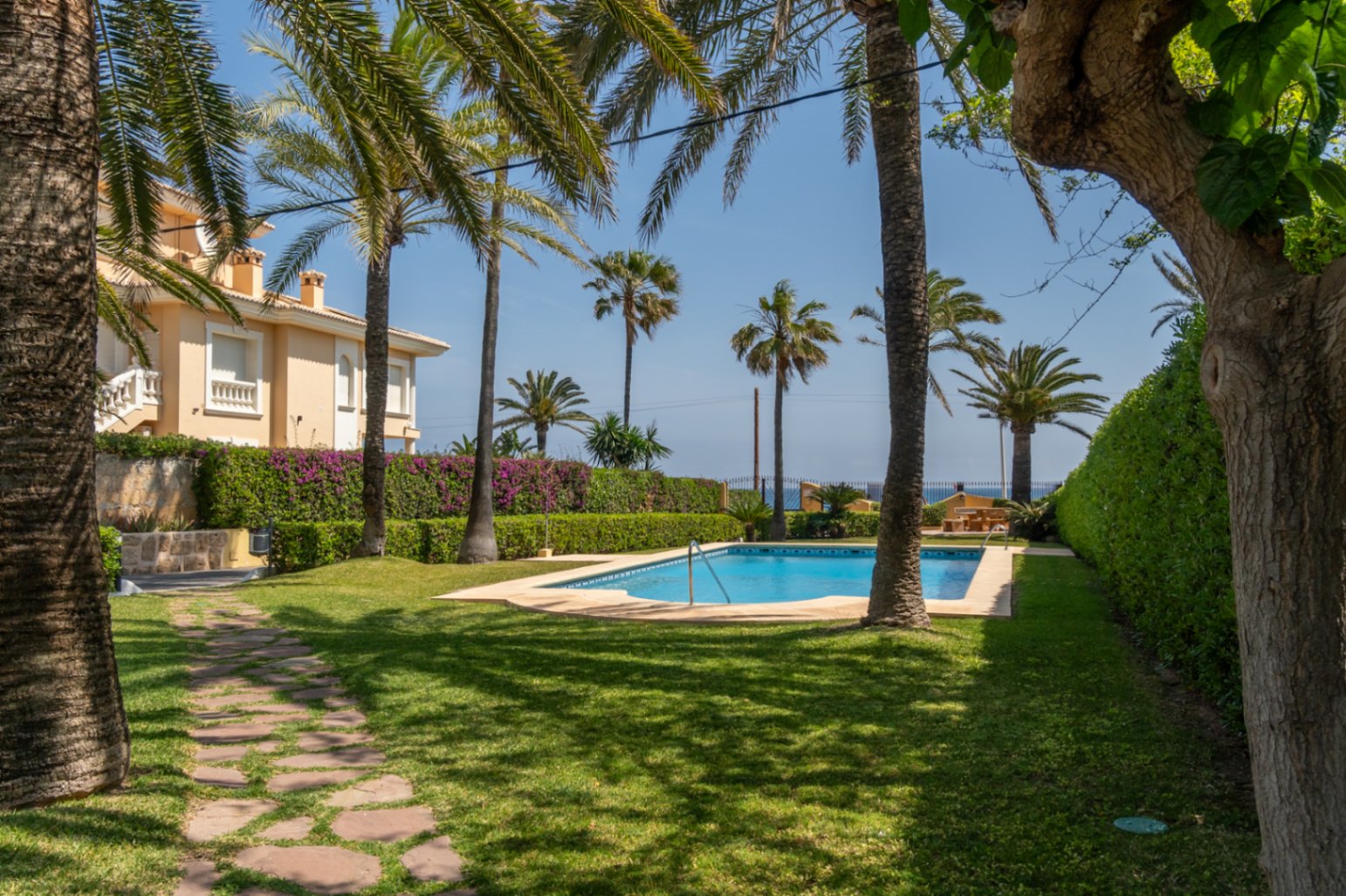 Vista de la piscina comunitaria rodeada de césped y palmeras en una urbanización de Jávea.