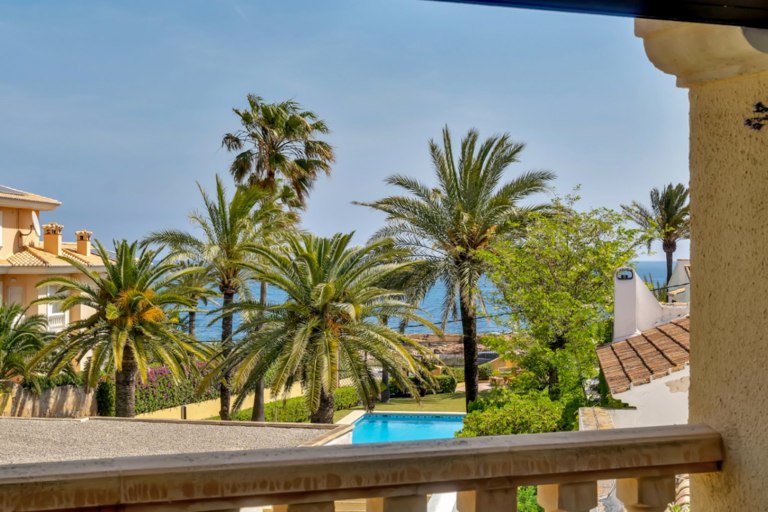 Vistas desde la terraza a la piscina comunitaria y el mar Mediterráneo, rodeado de palmeras.
