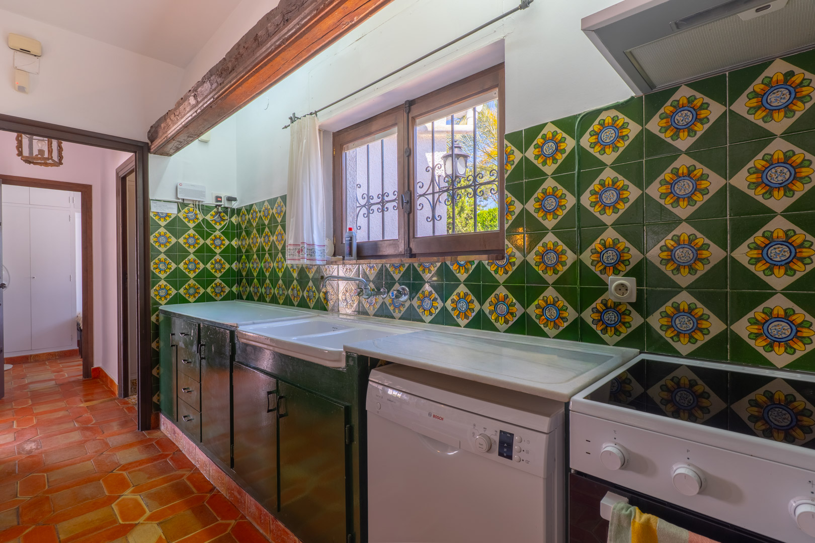 Cocina rústica con azulejos decorativos, encimera de mármol y suelo de terracota.