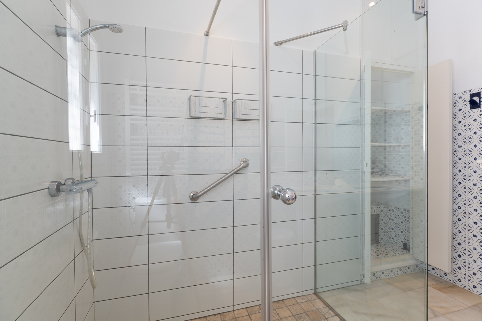 Detalle de la ducha con mampara de cristal y azulejos blancos con sutiles diseños.