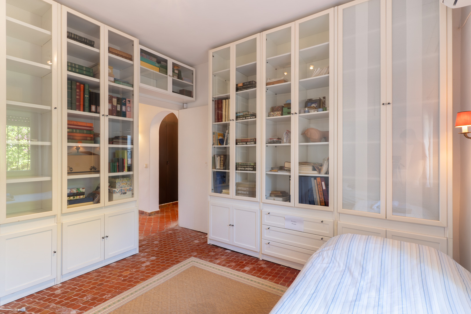 Dormitorio con estanterías blancas empotradas y suelo de terracota.