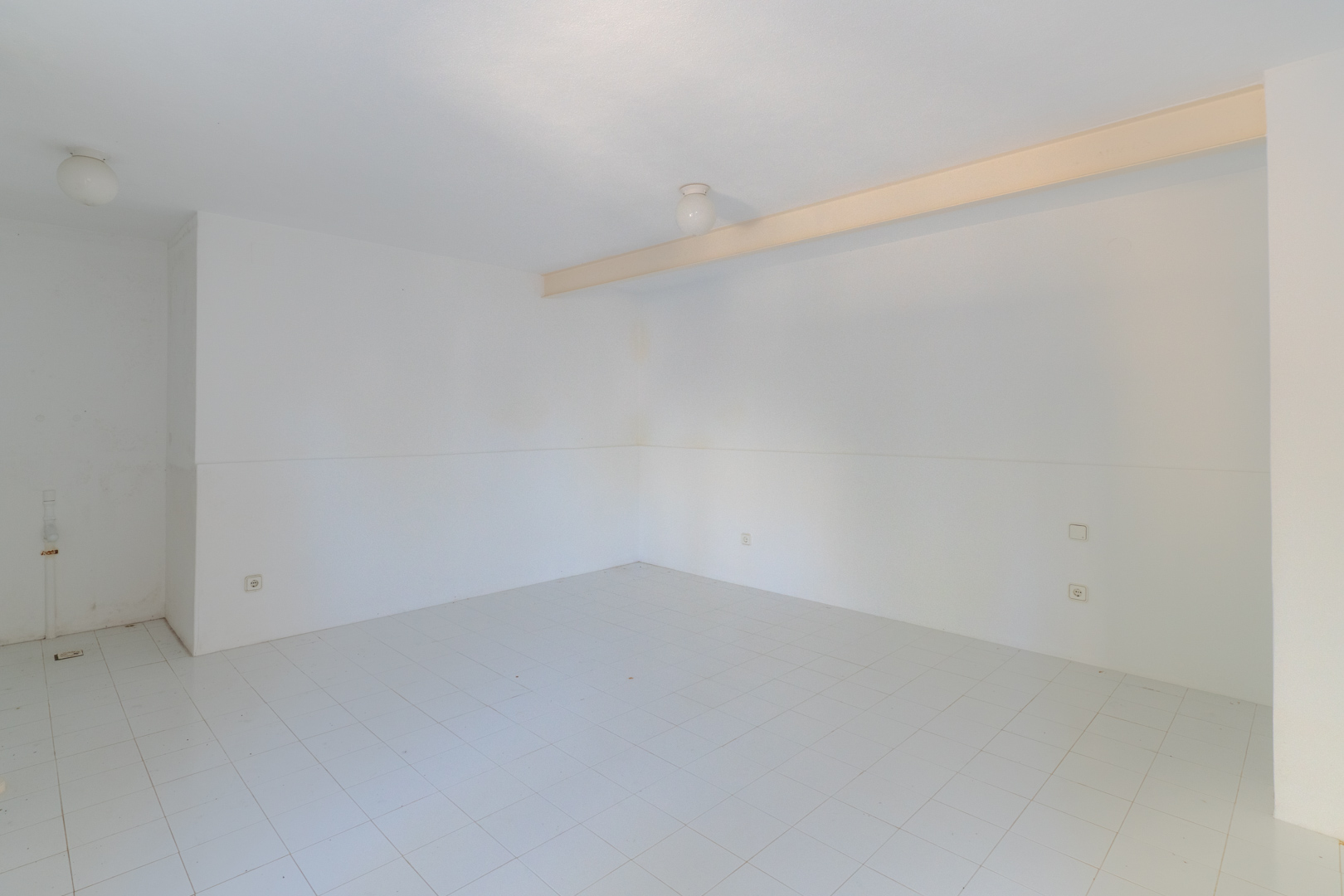 Espacio diáfano con paredes blancas, suelo de baldosas y luz cenital.