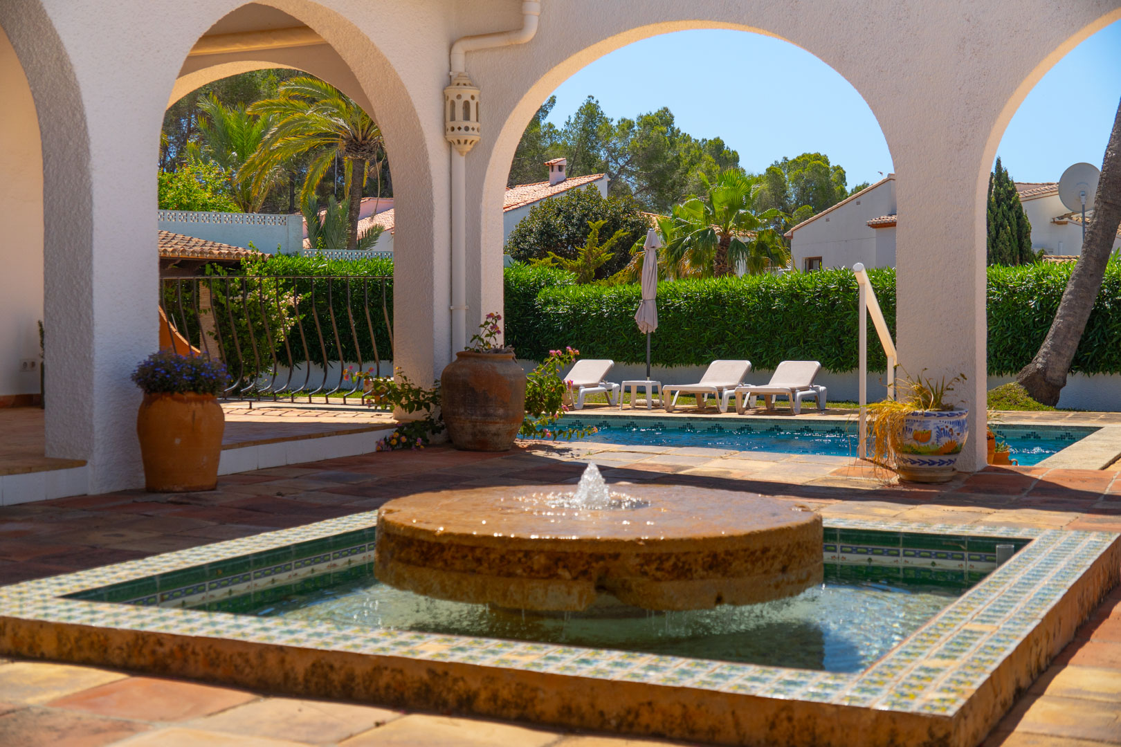 Fuente de piedra con mosaicos en patio con arcos y piscina.