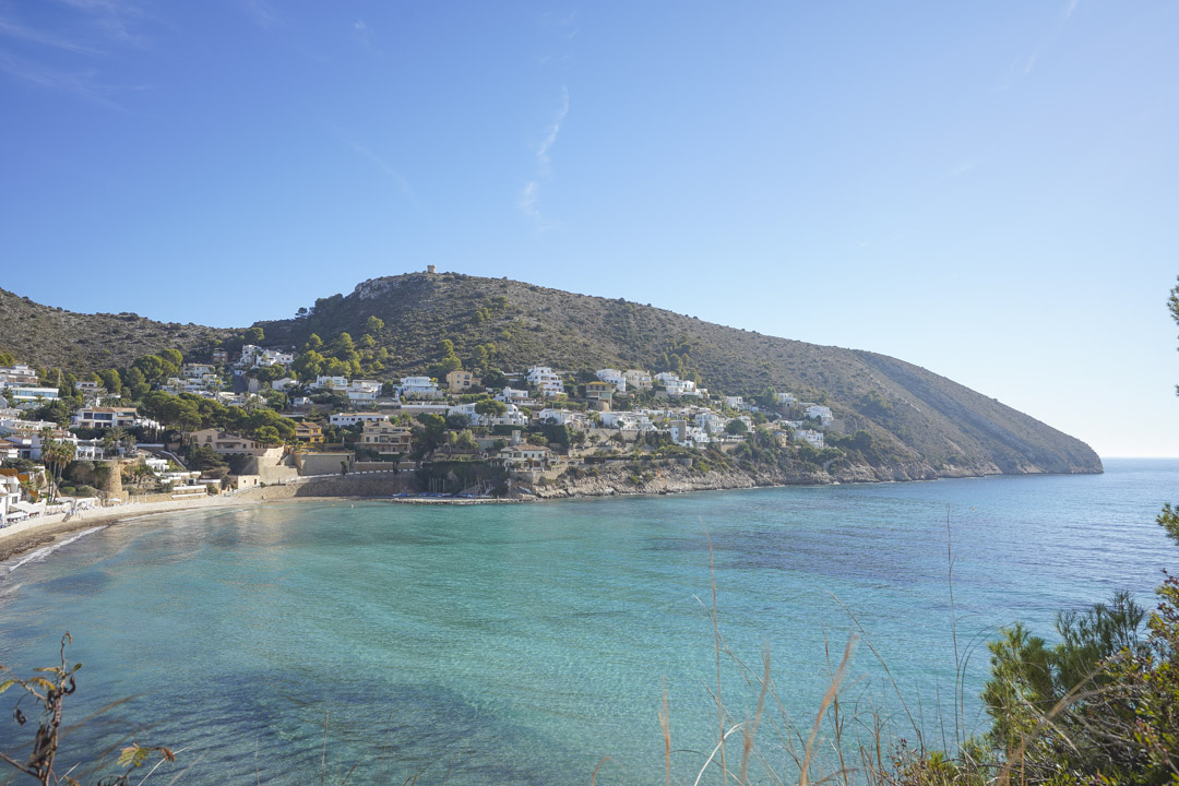 Vista panorámica de la costa de Moraira con aguas turquesas y casas blancas en la ladera.