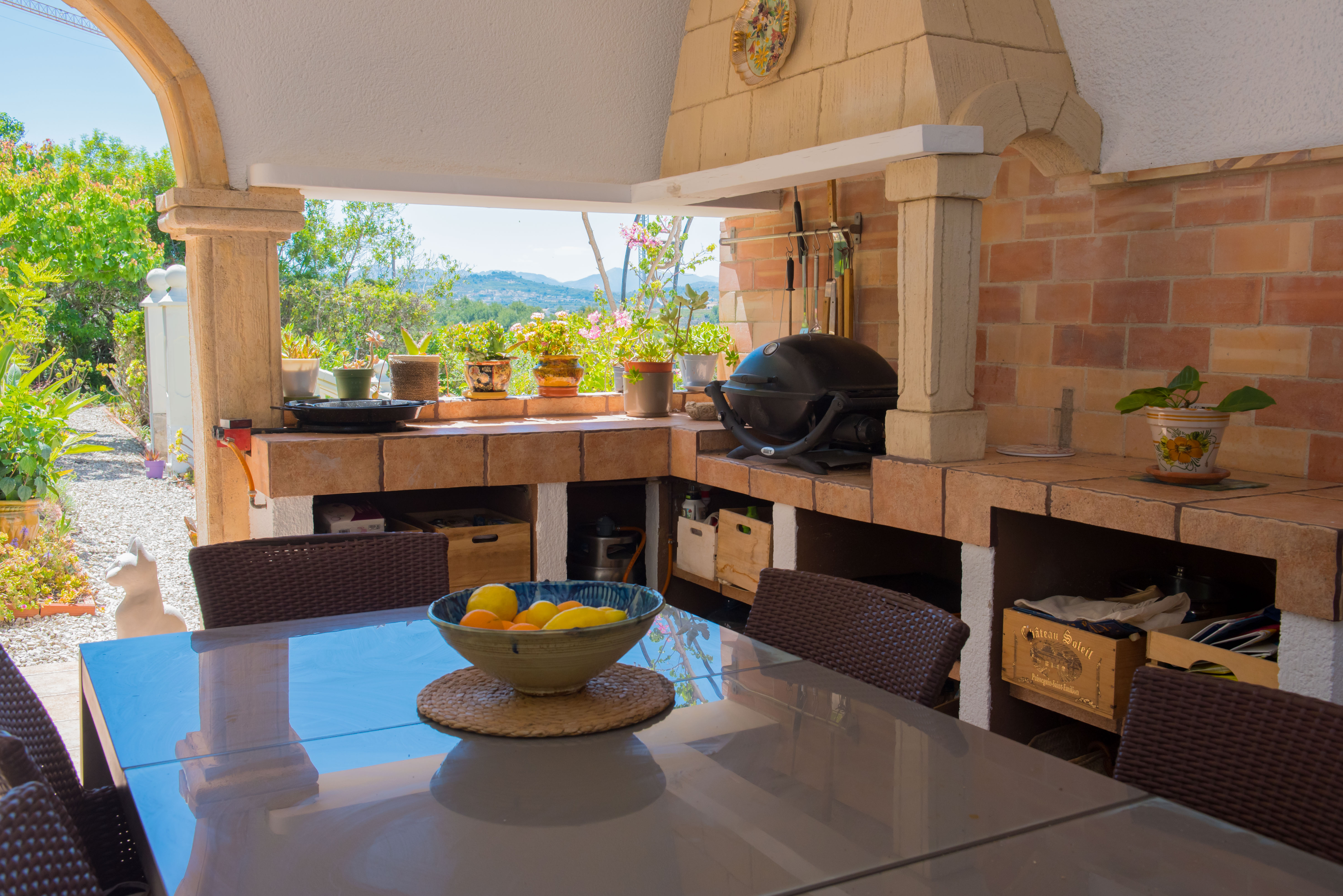 Barbacoa exterior con horno de ladrillo y mesa de comedor con vistas al jardín.