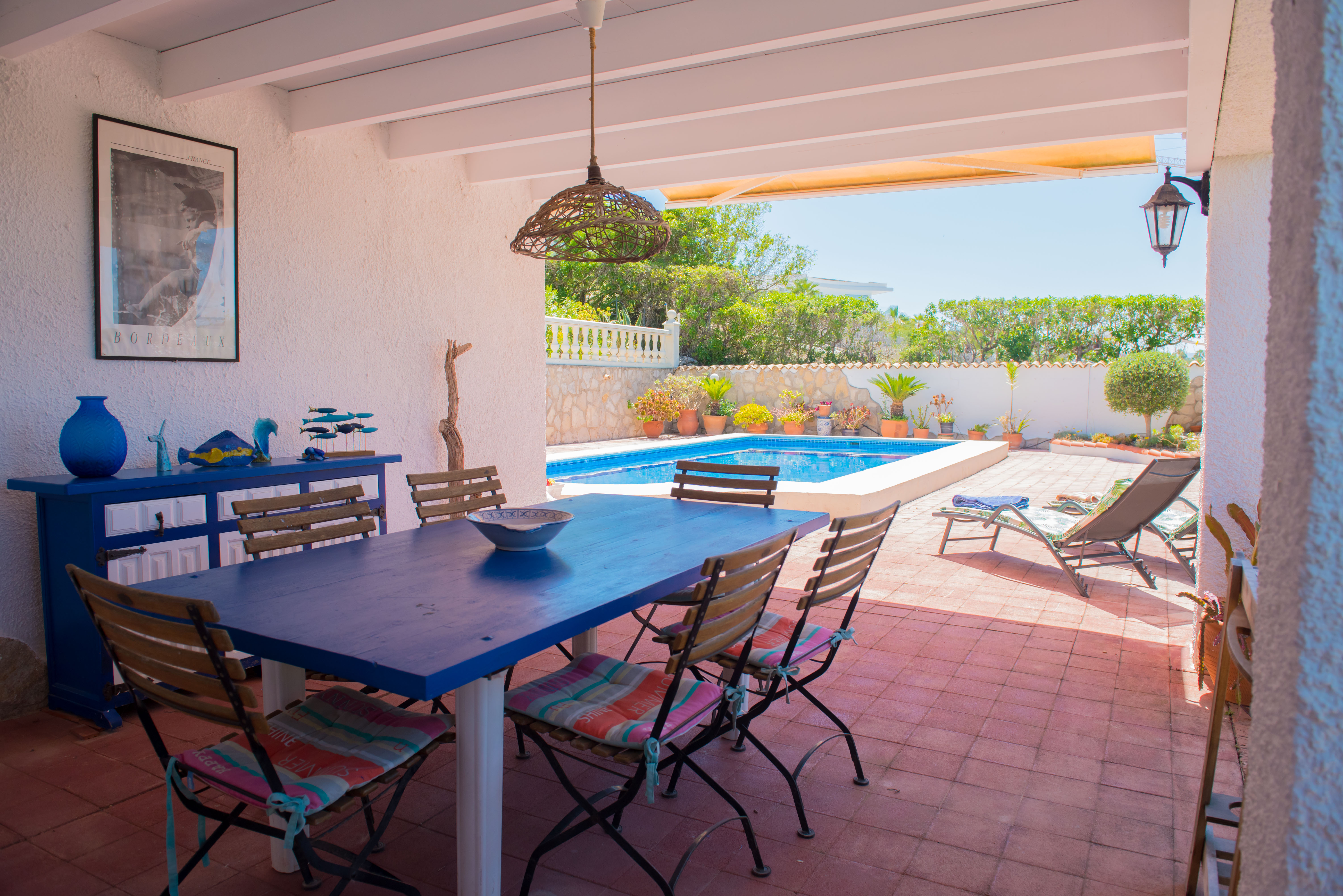 Comedor cubierto con mesa azul y vistas a la piscina.