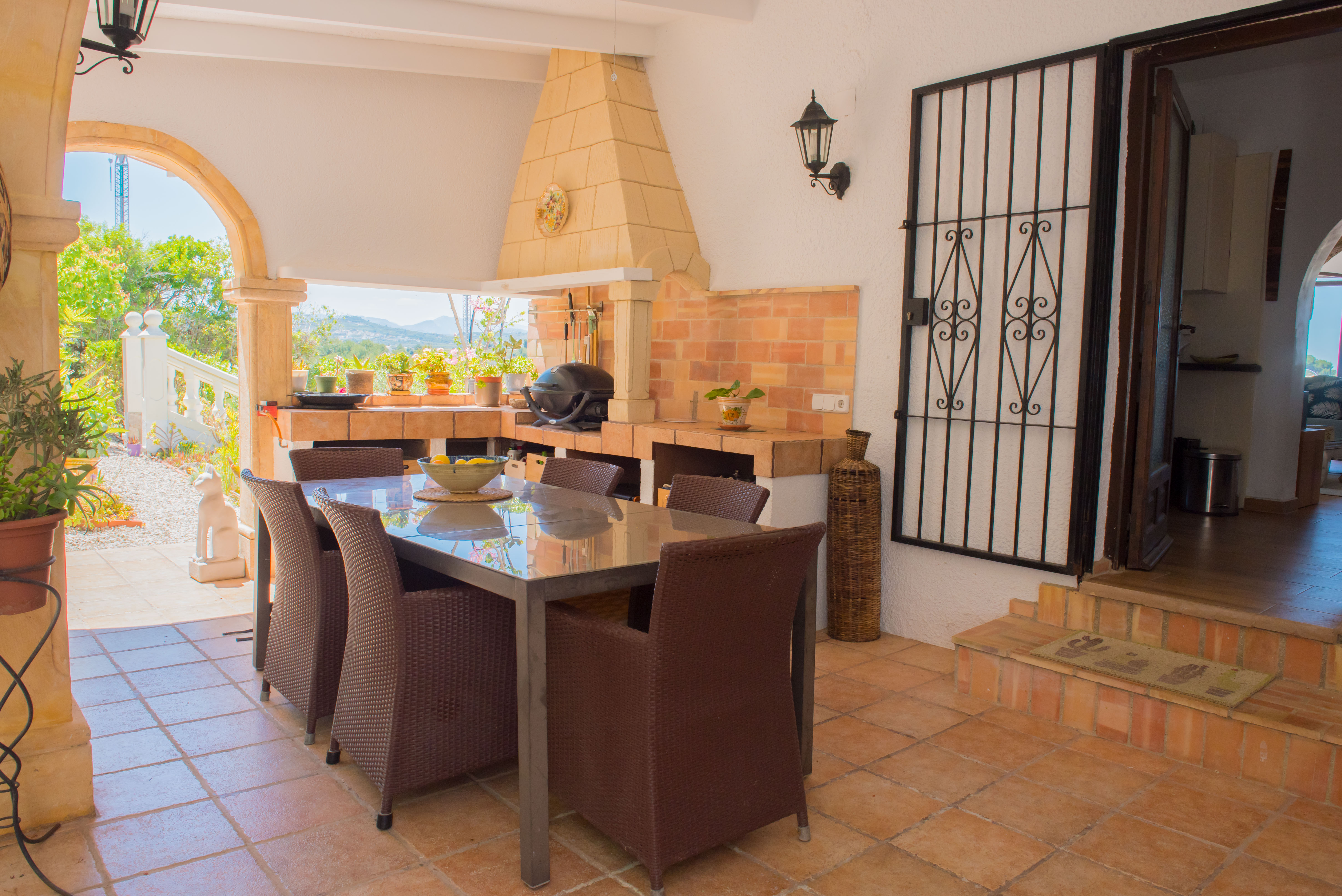 Comedor exterior cubierto con barbacoa de ladrillo visto y mesa de acero inoxidable.
