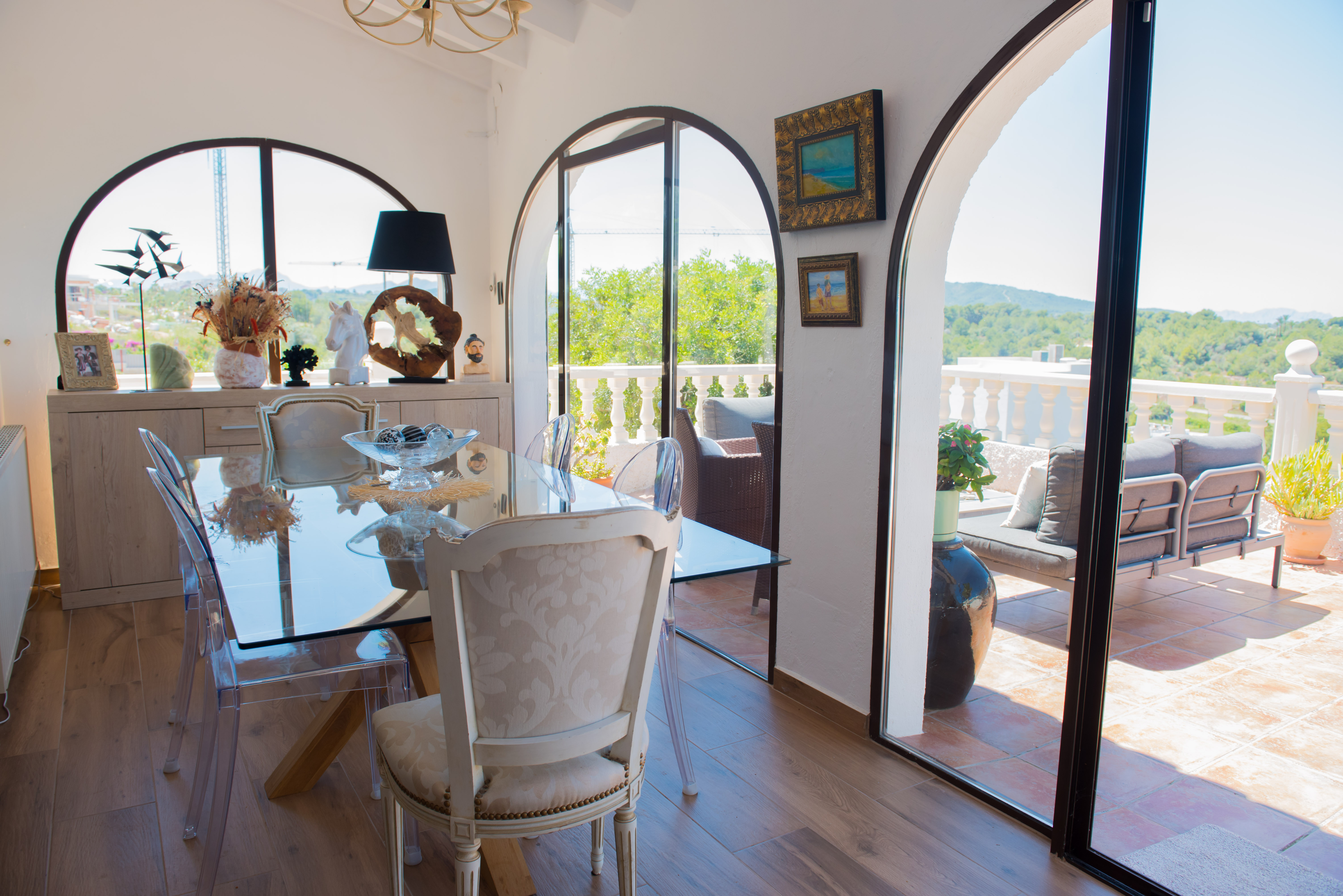 Comedor luminoso con mesa de cristal y acceso a terraza con vistas arboladas.