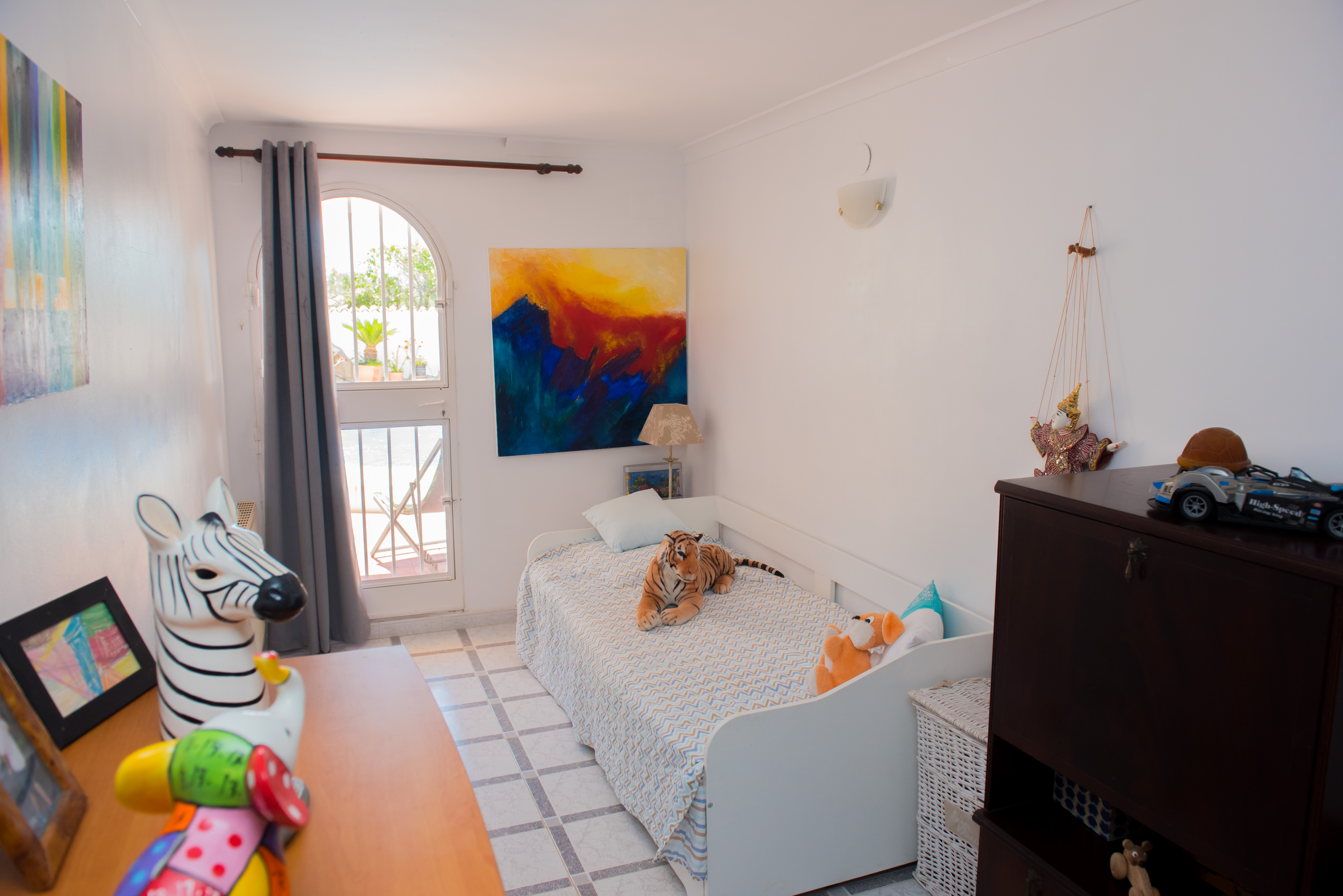 Habitación luminosa con cama individual, decoración colorida y acceso al exterior.