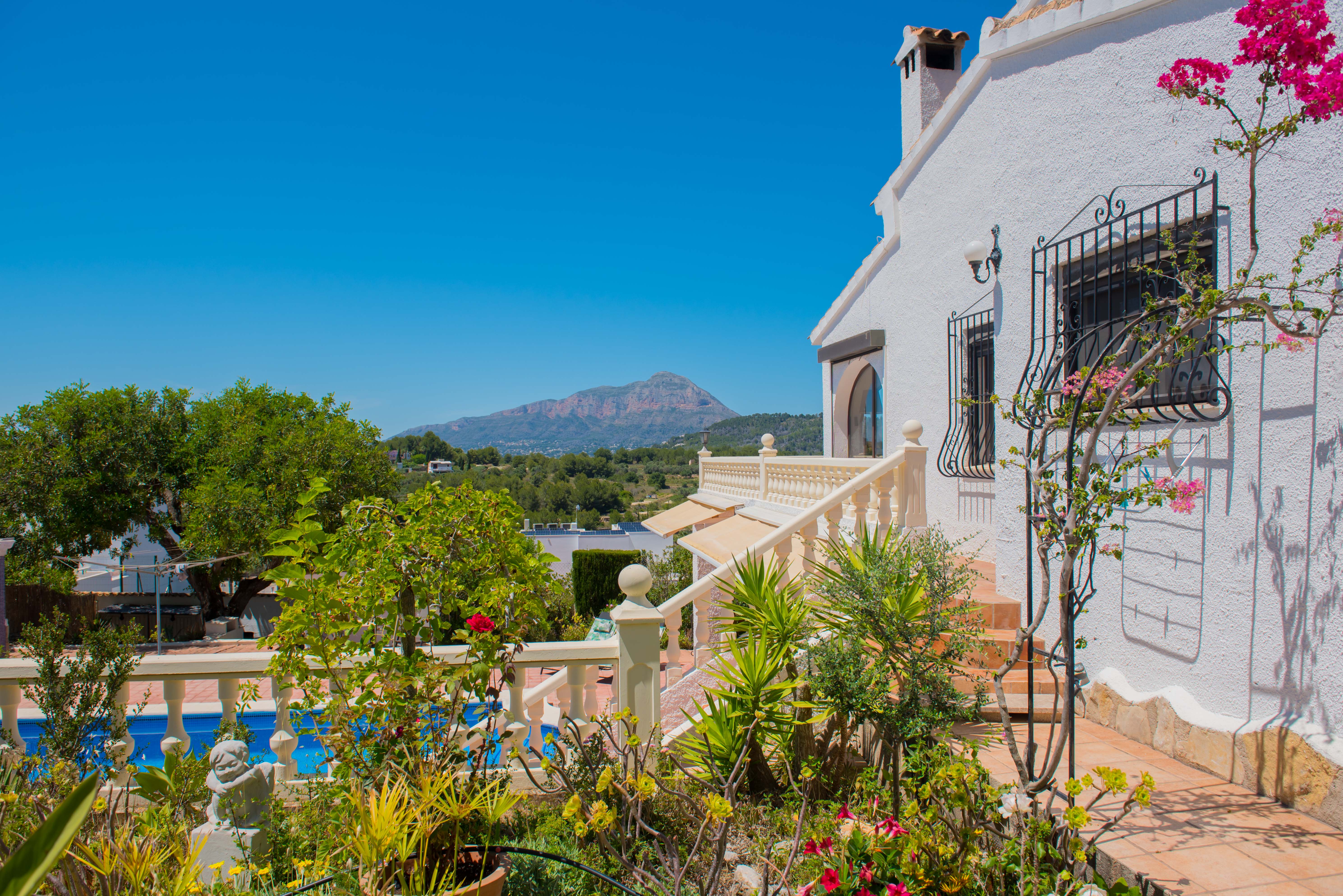 Jardín mediterráneo con piscina y vistas a la montaña desde la terraza.