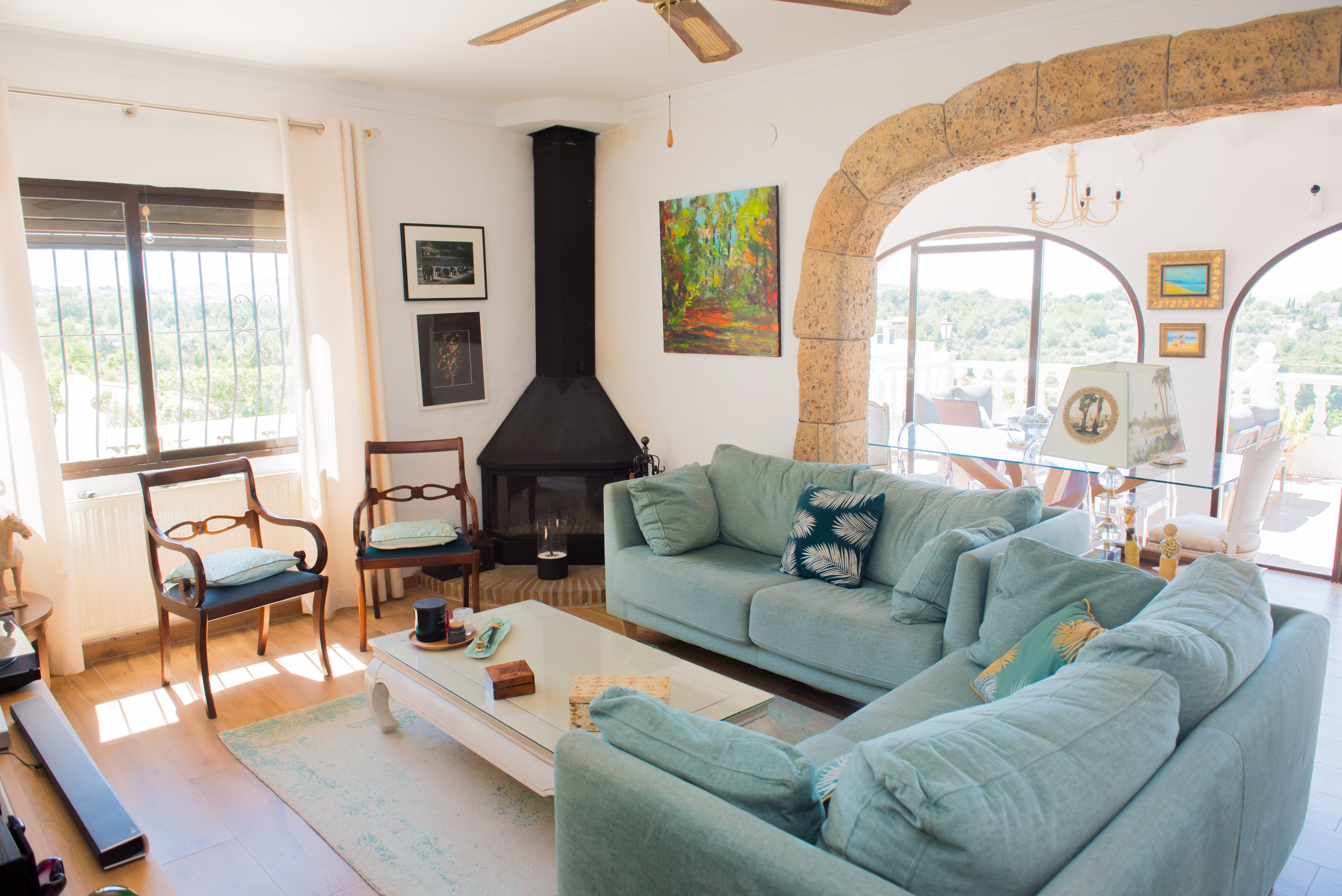 Salón con chimenea negra, sofá azul y arco de piedra que conecta con el comedor exterior.
