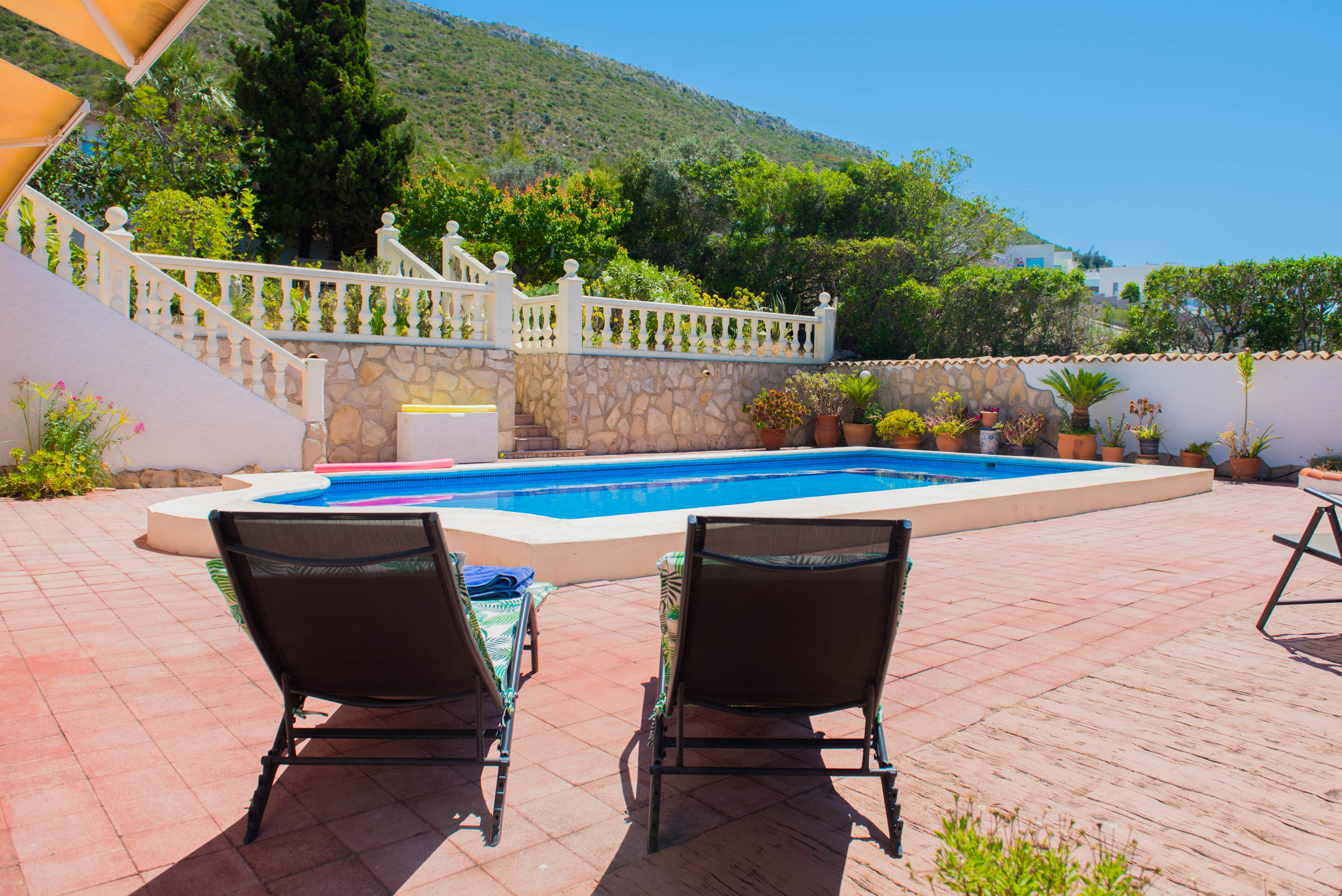 Vista de la piscina rectangular con baldosas rojas y tumbonas, rodeada de vegetación exuberante.