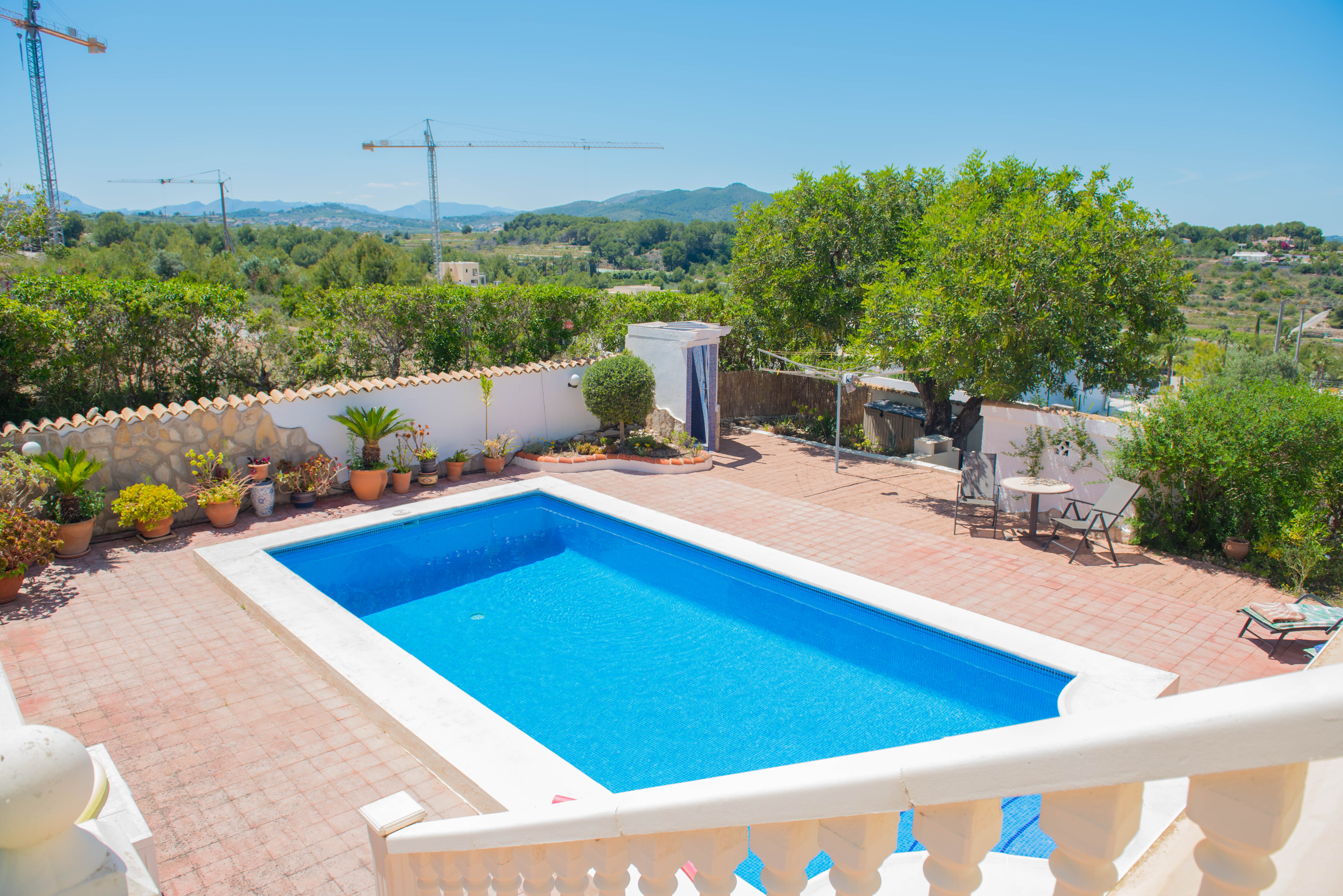 Vista elevada de la piscina rectangular con borde blanco y patio de baldosas rojas.