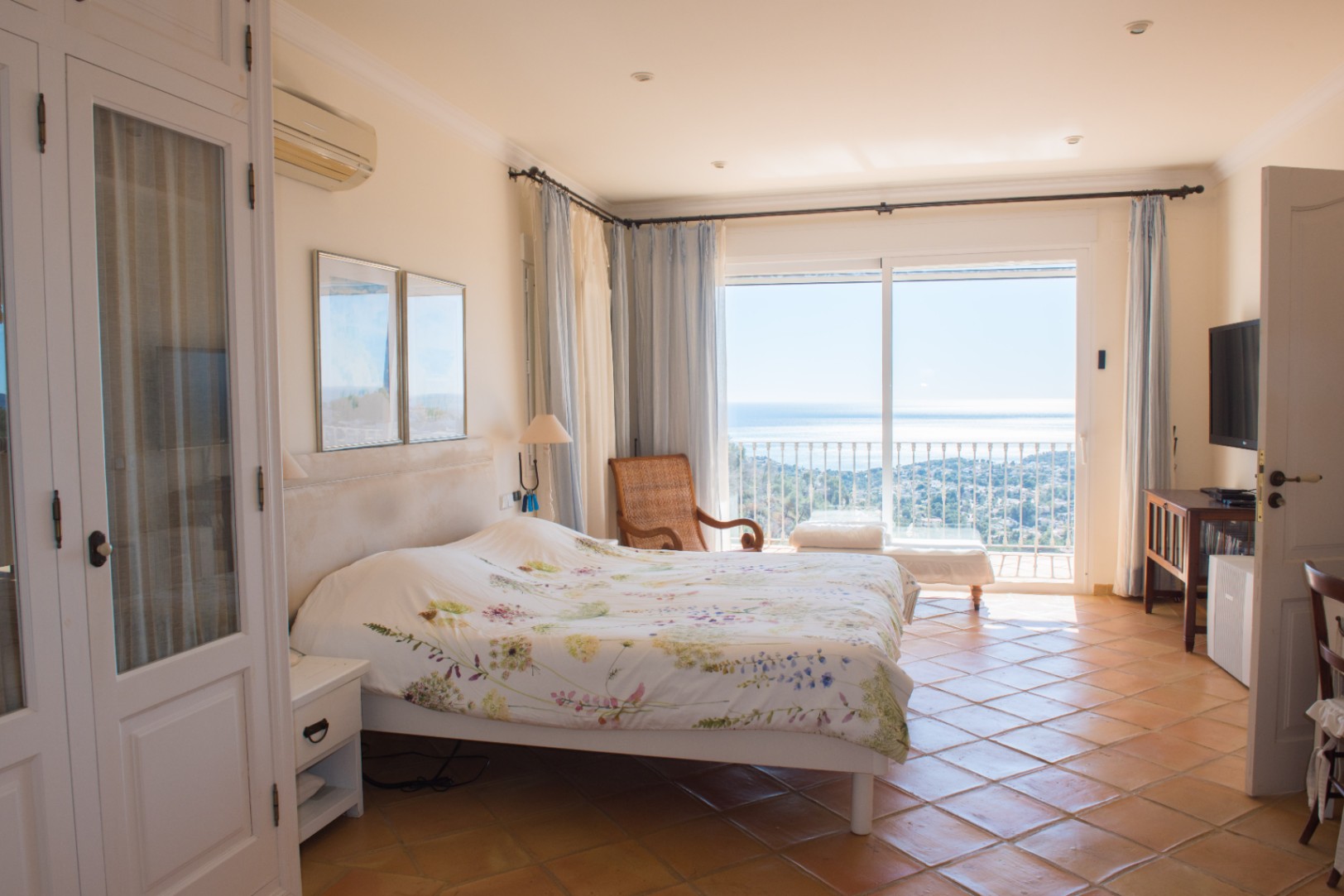 Dormitorio luminoso con suelos de terracota, armarios empotrados blancos y acceso directo a una terraza con vistas panorámicas al mar Mediterráneo.