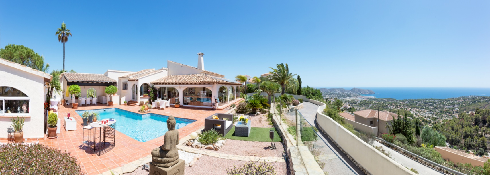 Terraza panorámica con baldosas de terracota, piscina privada y una estatua de Buda, con vistas despejadas al mar Mediterráneo y al paisaje costero.