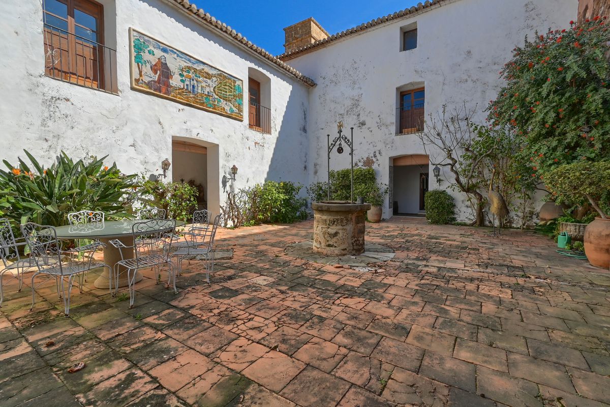 Patio interior tradicional con suelo de barro cocido, pozo central de piedra y un mural cerámico decorativo en las paredes encaladas de la finca.