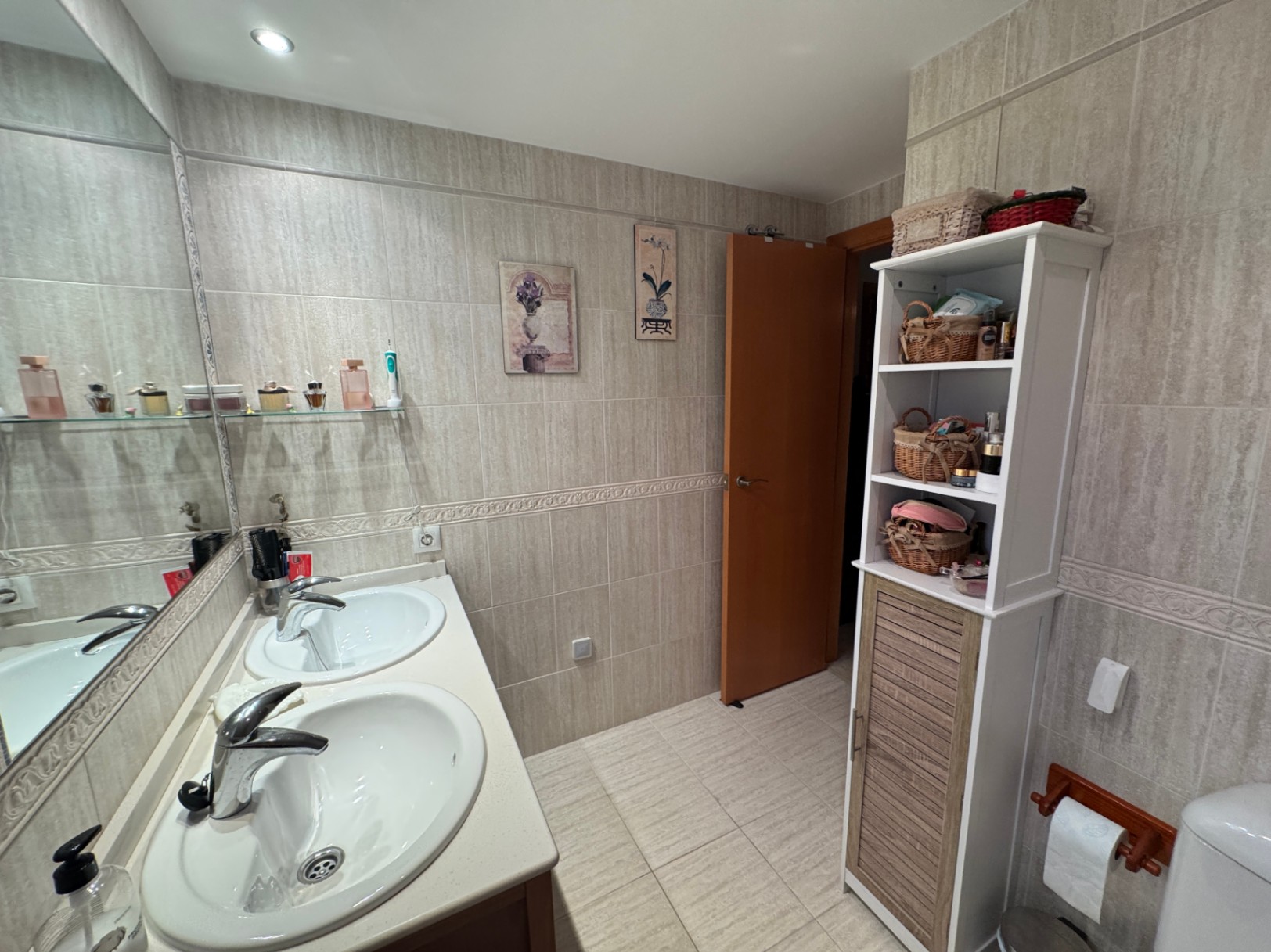 Cuarto de baño con lavabo doble, espejo y estantería de almacenamiento.