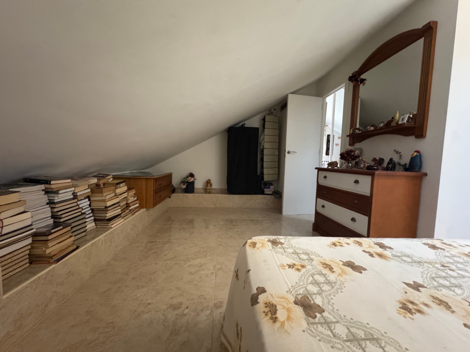 Dormitorio abuhardillado con estantería de libros integrada y cómoda de madera.