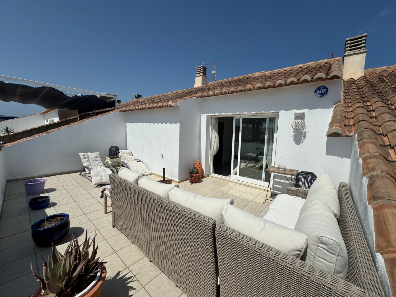 Terraza privada con suelo cerámico, mobiliario de ratán sintético y acceso directo mediante puertas correderas bajo un tejado de teja tradicional.