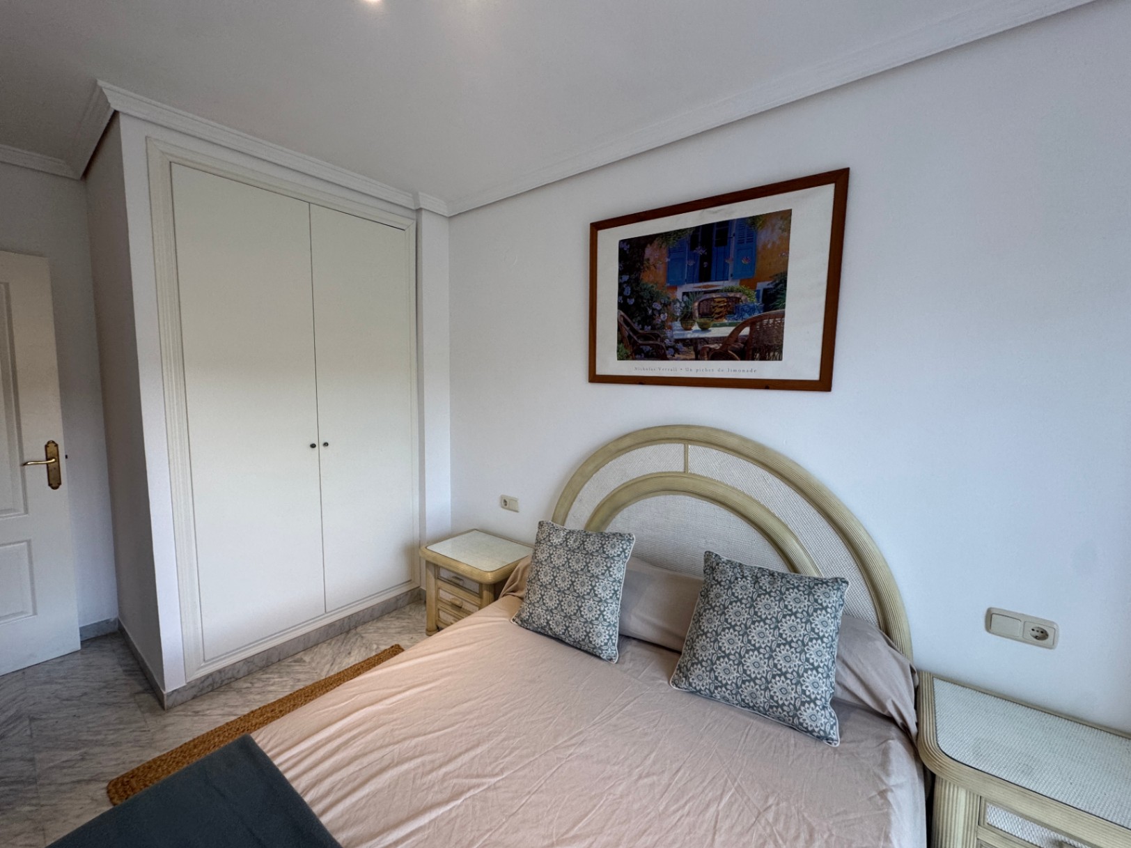Dormitorio con armario empotrado blanco, suelos de mármol y cama con cabecero curvo flanqueada por mesitas de noche a juego.