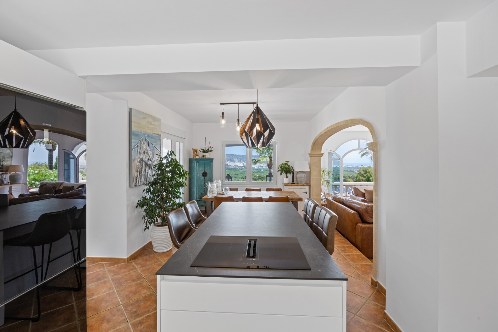 Isla de cocina moderna con placa de inducción integrada, suelos de terracota y un arco de piedra que conecta con el salón y ofrece vistas panorámicas al valle.