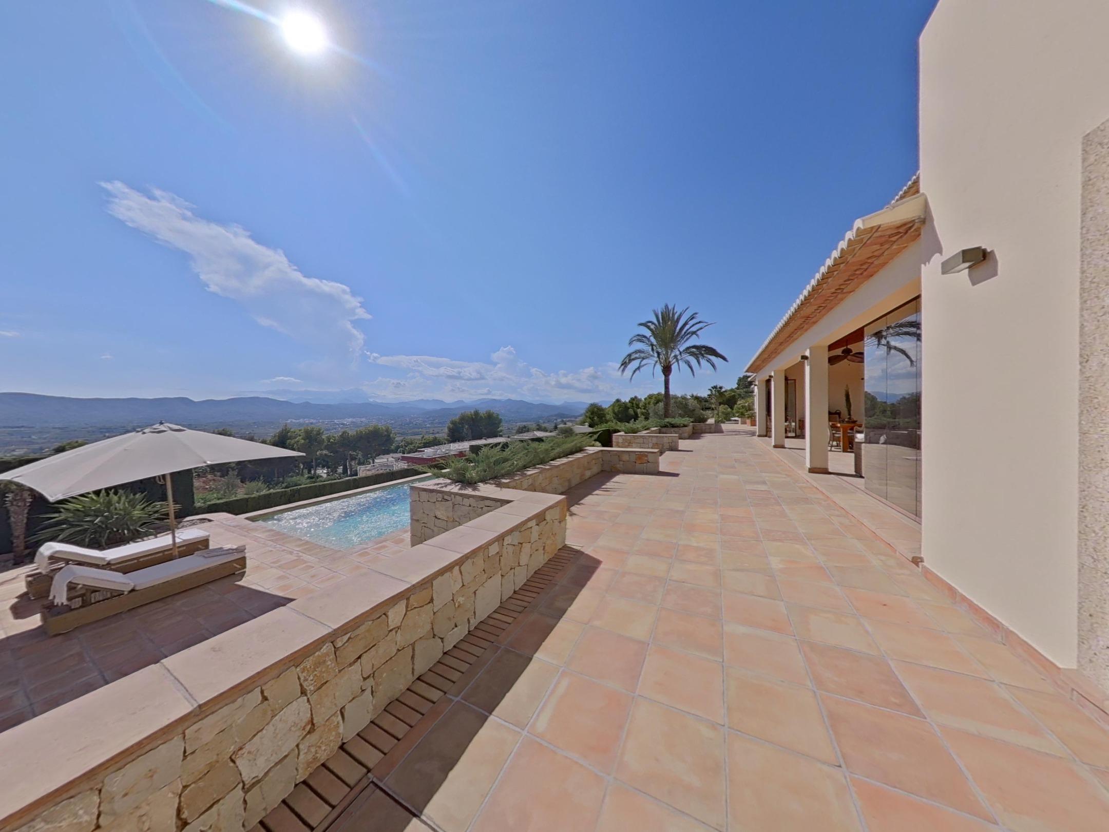 Amplia terraza de baldosas de terracota con muros de piedra natural y zona de piscina con vistas panorámicas al valle y las montañas.