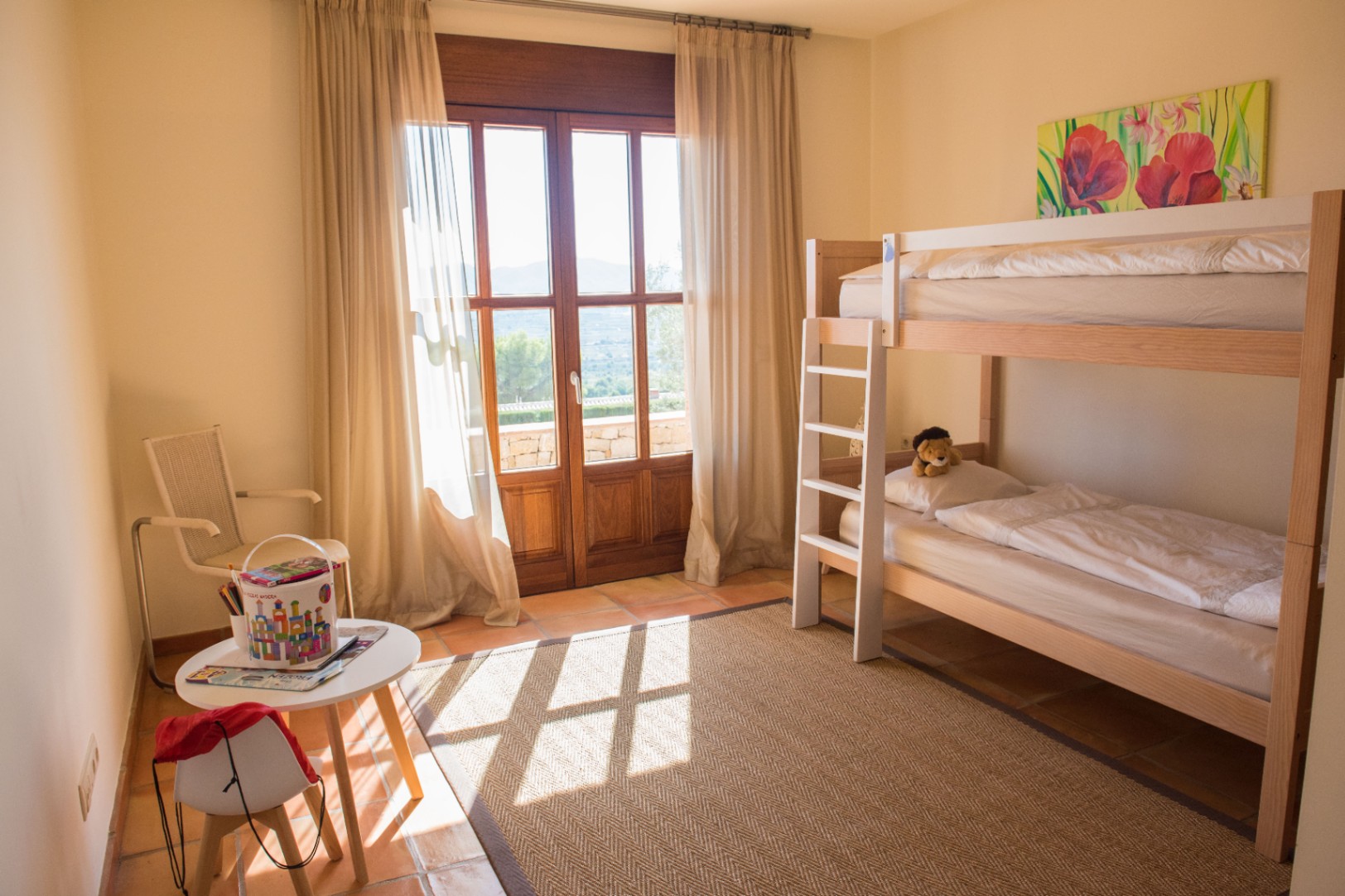 Dormitorio infantil con literas de madera, suelo de terracota y una puerta acristalada que ofrece acceso directo a una terraza con vistas despejadas.