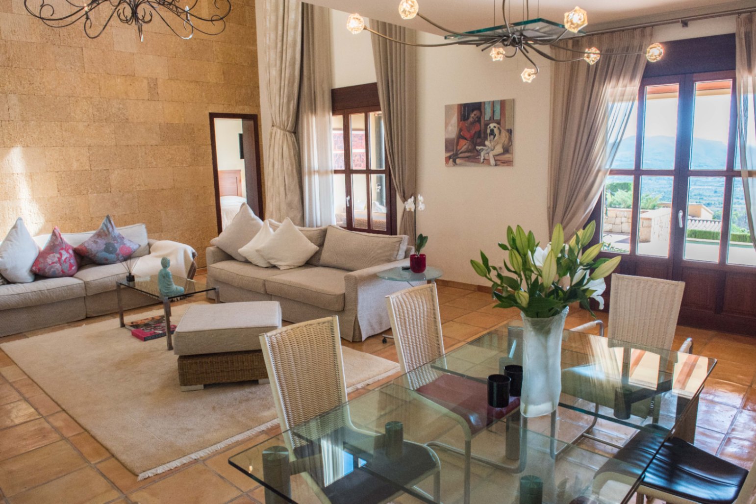 Salón-comedor de planta abierta con pared de piedra natural, suelos de terracota y amplios ventanales de madera que conectan con el exterior.