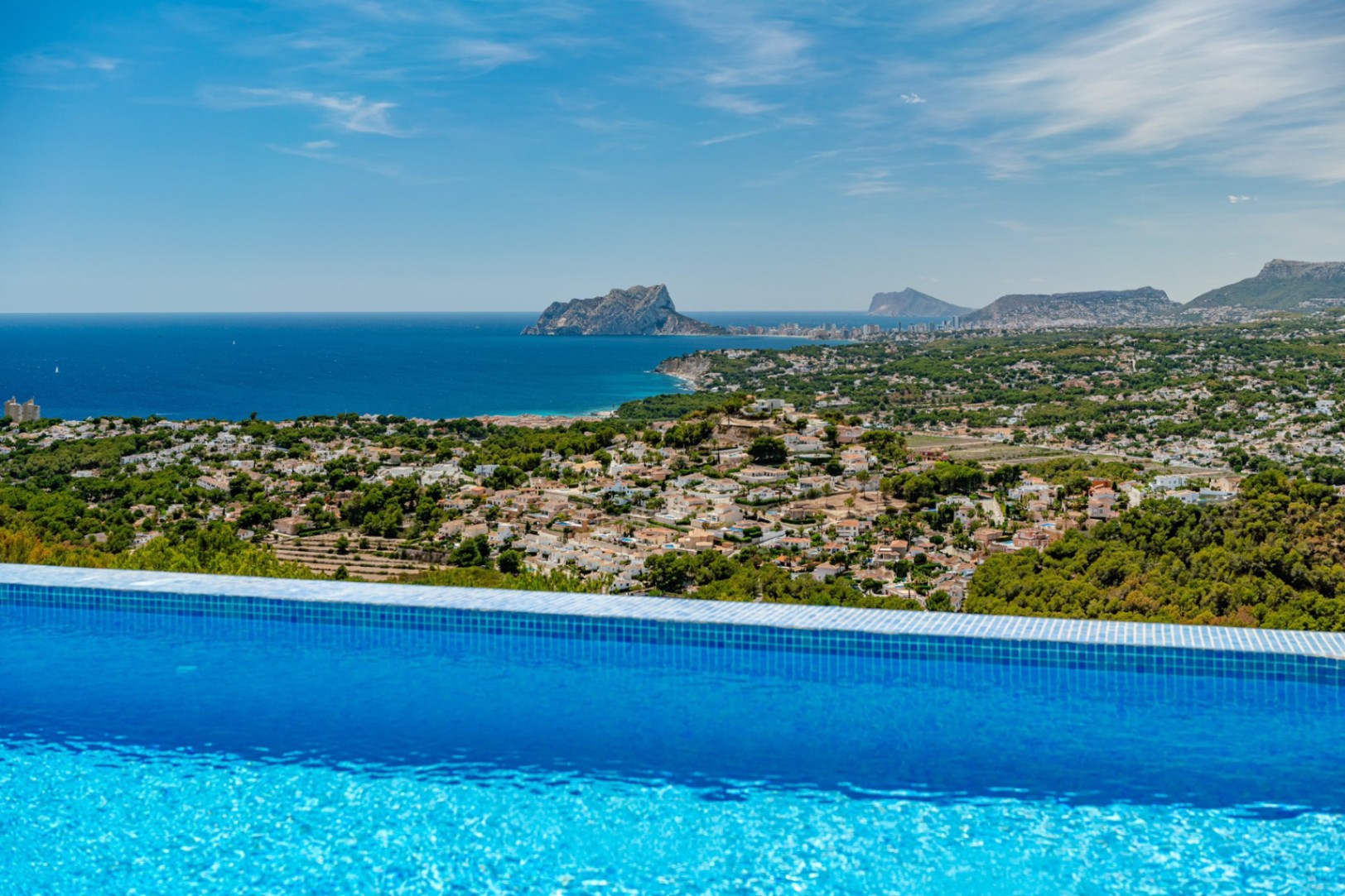 Piscina infinita con gresite azul y vistas panorámicas al Mediterráneo, destacando el Peñón de Ifach y el perfil costero de Calpe.