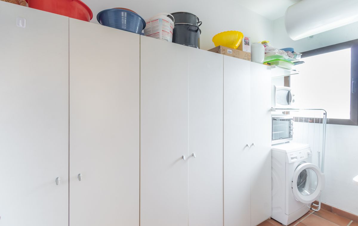 Cuarto de servicio con amplios armarios blancos, suelo de baldosa cerámica y zona de lavandería equipada con lavadora y electrodomésticos auxiliares.