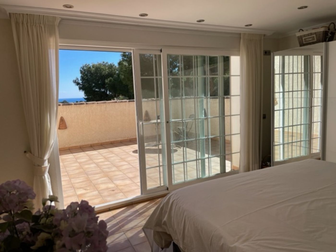 Dormitorio con grandes puertas correderas de cristal que dan acceso a una terraza privada con vistas al mar y mobiliario de exterior.