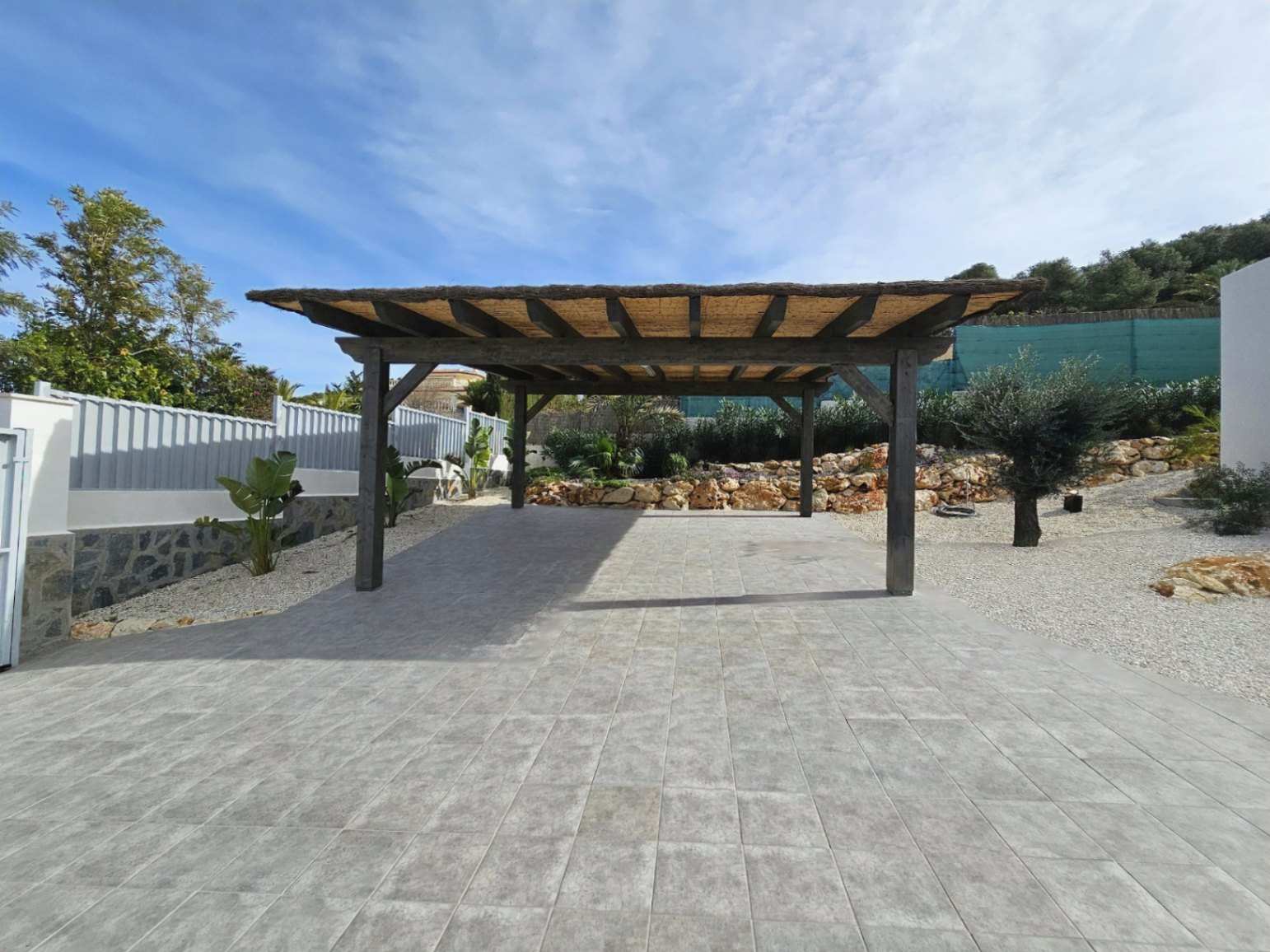 Pérgola de madera con cubierta de paja sobre suelo de baldosas grises en el área de estacionamiento.