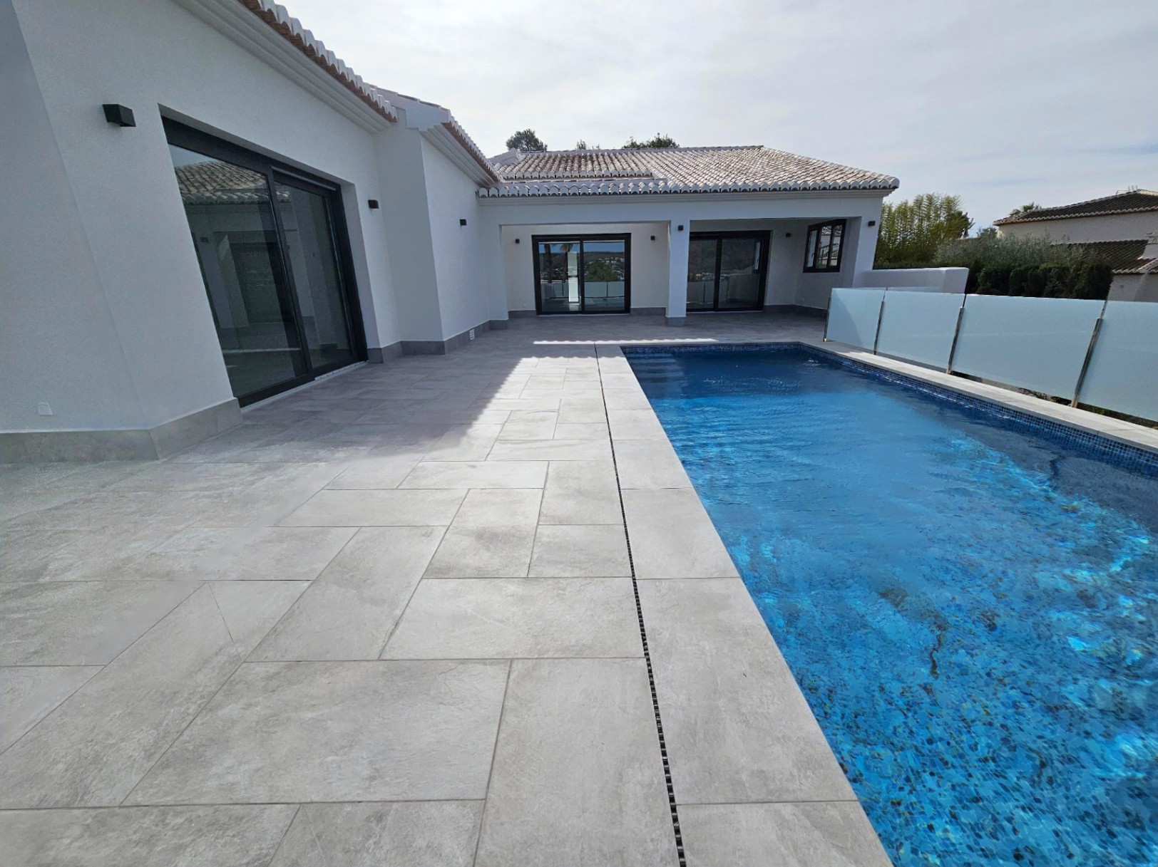 Vista de la terraza pavimentada con piscina y barandilla de cristal.