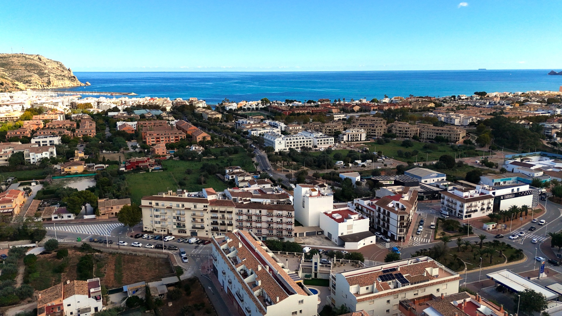 Vista panorámica elevada del casco urbano de Jávea, mostrando la arquitectura mediterránea, la zona del puerto y el mar azul bajo un cielo despejado.
