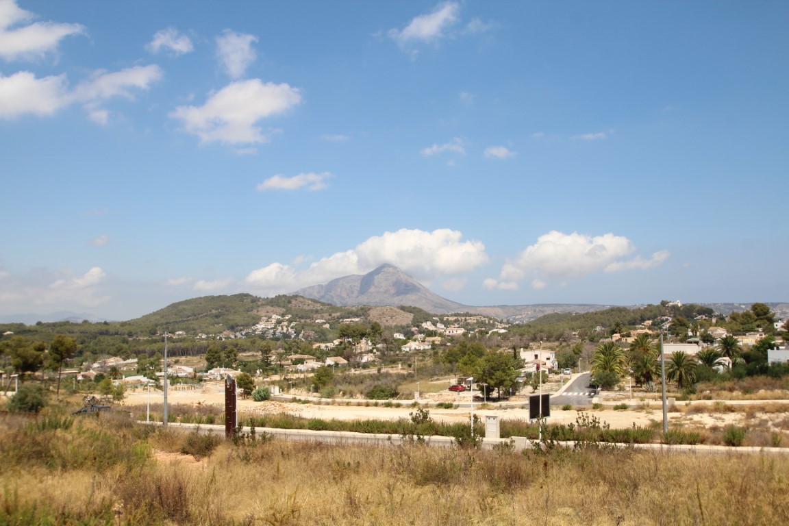 Vista de parcelas edificables con el Montgó al fondo, bajo un cielo azul con nubes dispersas.