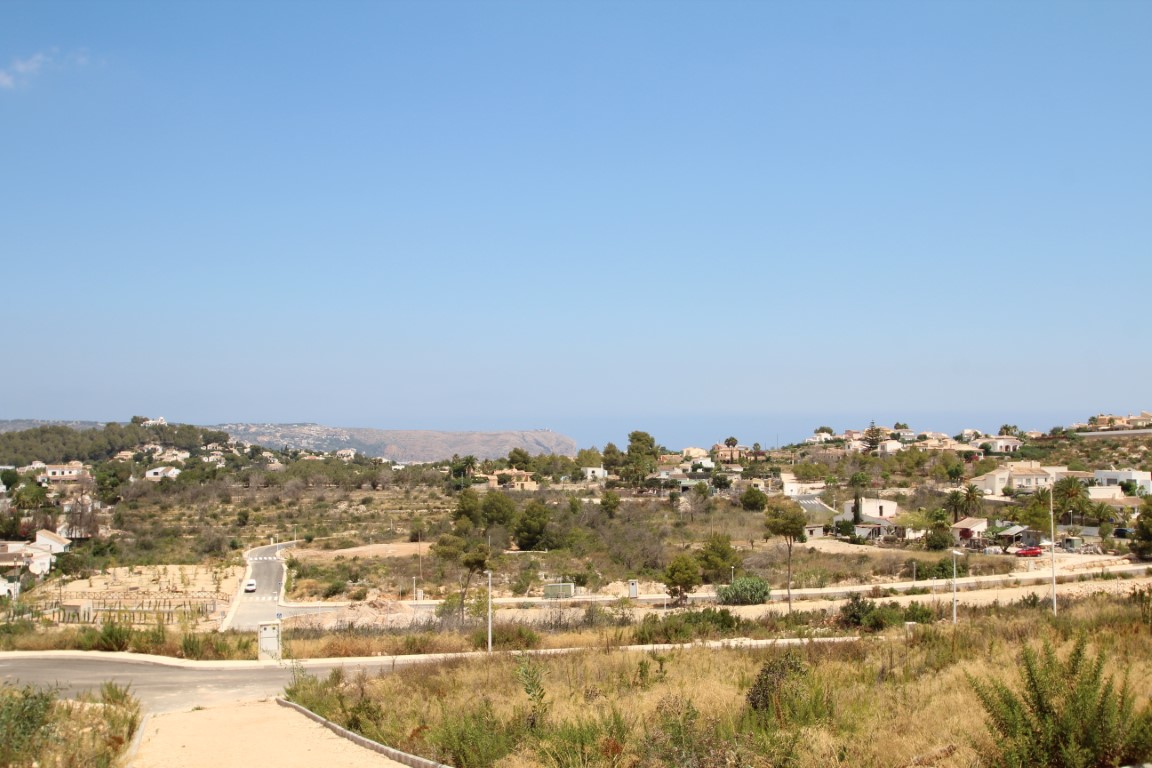 Vista panorámica de la urbanización con casas dispersas y vegetación autóctona, bajo un cielo azul despejado.