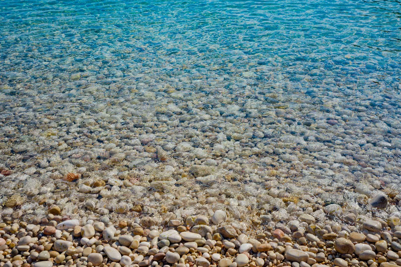 Vista detallada de las aguas cristalinas y los cantos rodados blancos de la playa de la Granadella, situada en el entorno natural cercano a la villa en Jávea.