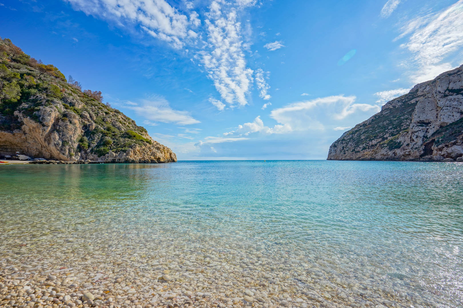 Vista panorámica de la Playa de la Granadella en Jávea, destacando sus aguas cristalinas, orilla de guijarros blancos y acantilados con vegetación mediterránea.