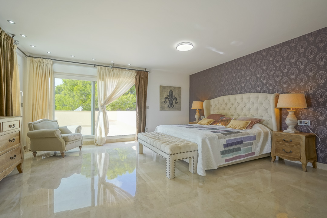 Dormitorio principal con suelos de mármol pulido, pared de acento con papel tapiz estampado y acceso directo a la terraza a través de amplios ventanales.