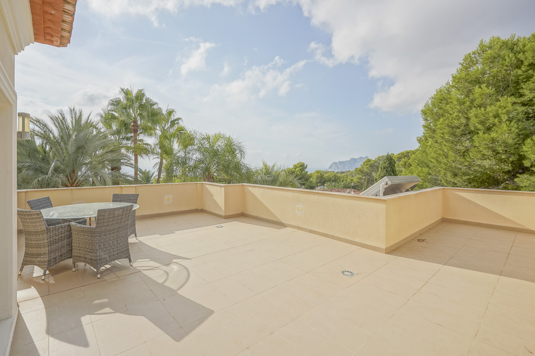Terraza superior con suelo cerámico y mobiliario de exterior, ofreciendo vistas despejadas al Peñón de Ifach y a la vegetación mediterránea circundante.