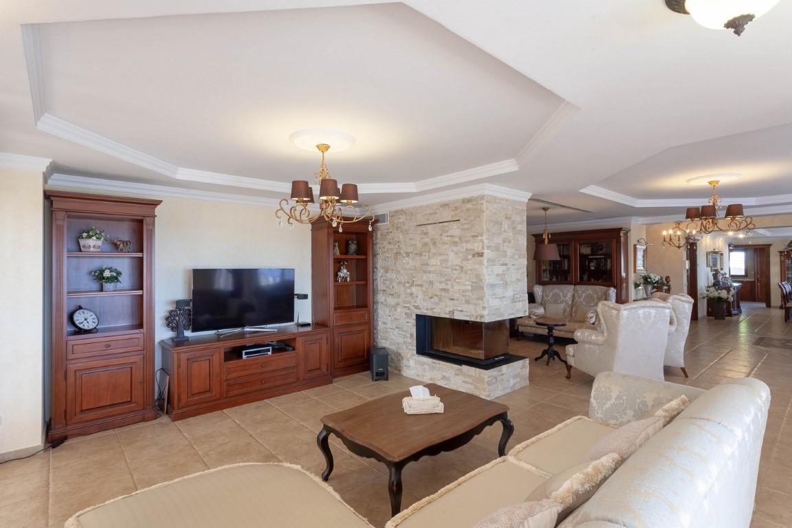 Salón principal con dos zonas de estar independientes, chimenea central revestida de piedra natural, mobiliario de madera clásica y suelos cerámicos.