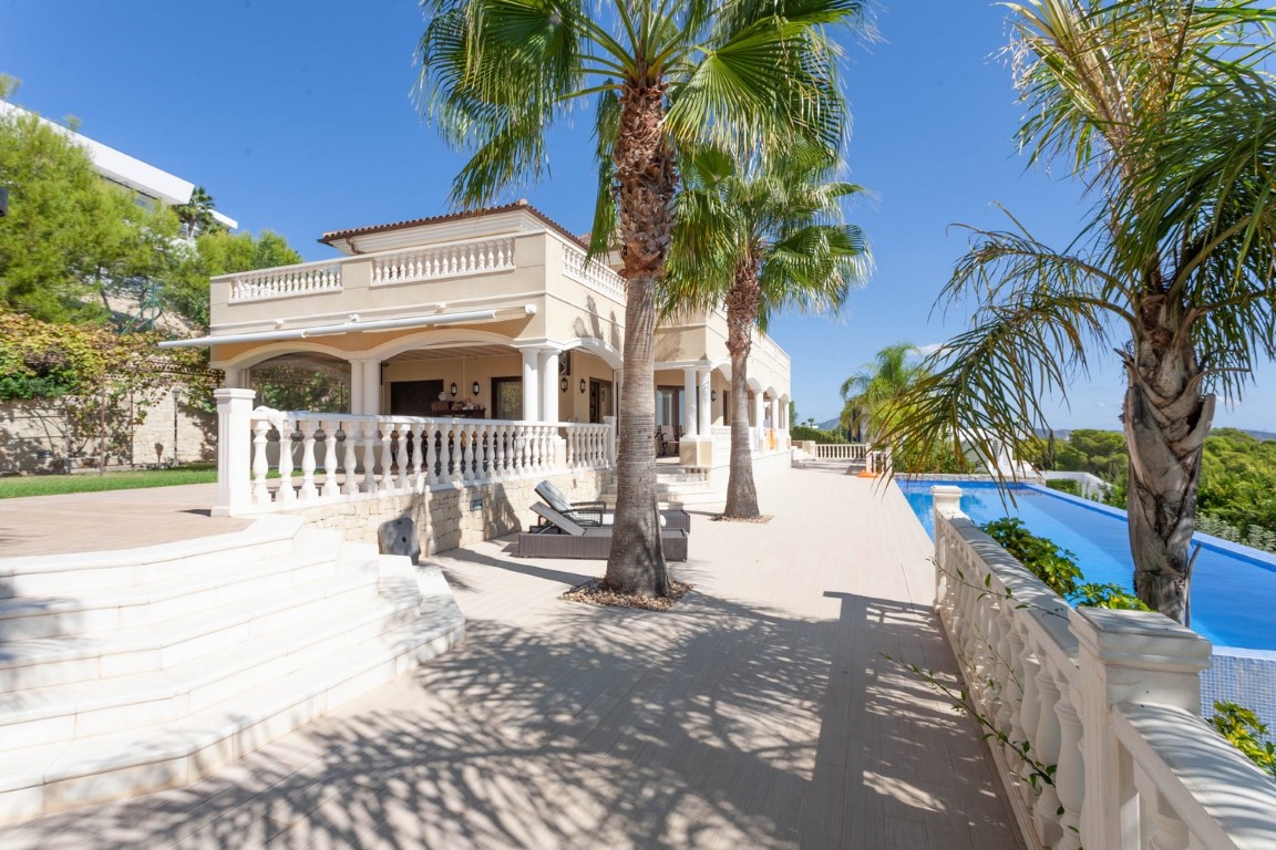 Terraza exterior con balaustrada clásica, palmeras y una piscina infinita alargada junto a la fachada de estilo mediterráneo con arcos y balcones.