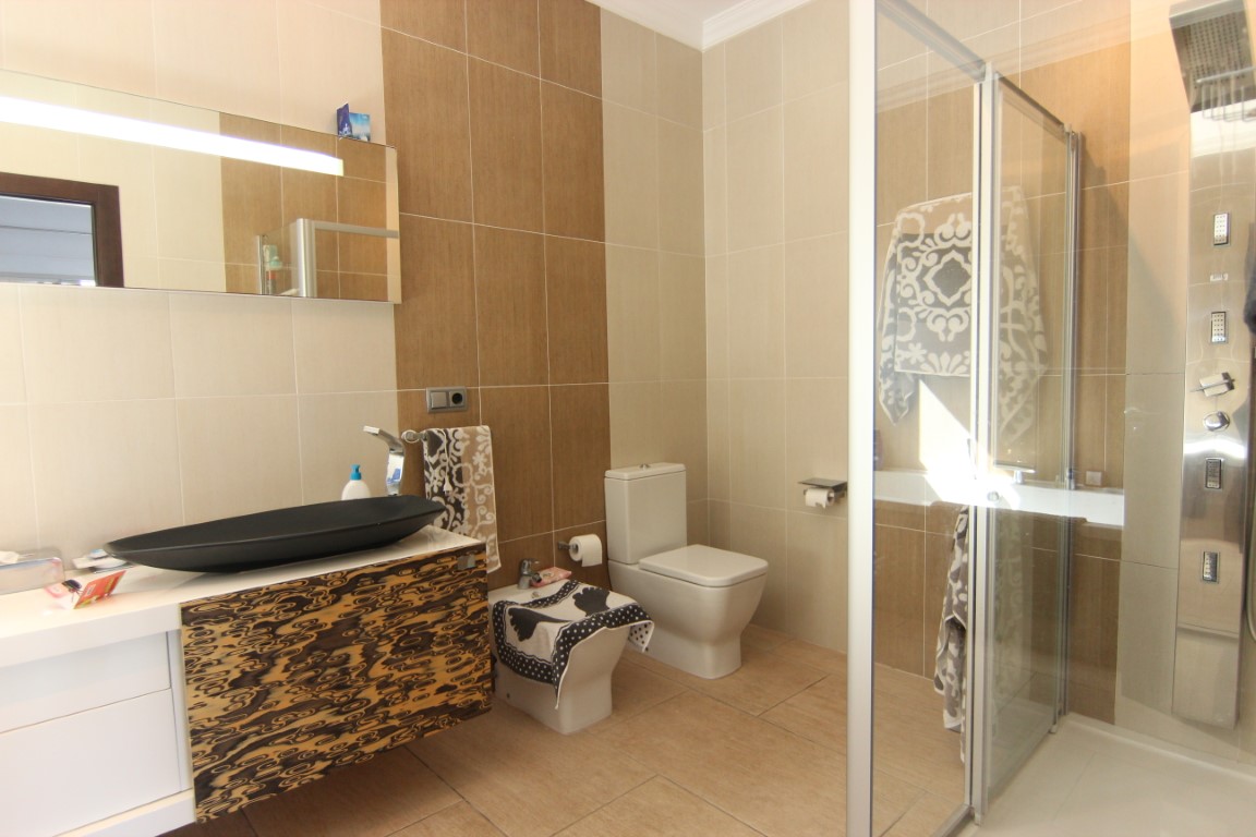 Baño moderno con lavabo de diseño negro, mueble suspendido con frontal texturizado y ducha con panel de hidromasaje integrado.