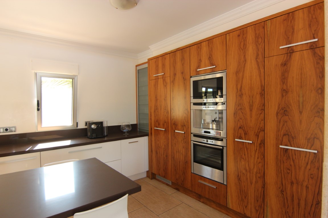 Cocina espaciosa con armarios de madera natural, electrodomésticos integrados de acero inoxidable y encimera oscura en contraste con muebles blancos.