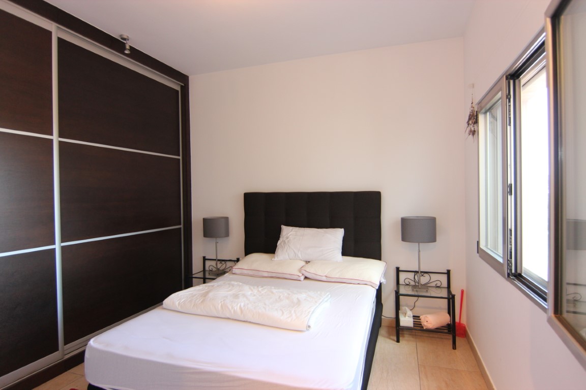 Dormitorio doble con amplio armario empotrado de madera oscura, mesas de noche minimalistas y luz natural proveniente del ventanal lateral.