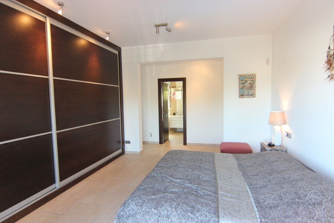 Dormitorio doble con amplio armario empotrado de madera oscura y puertas correderas. Incluye baño en suite integrado, suelos cerámicos y focos de techo ajustables.