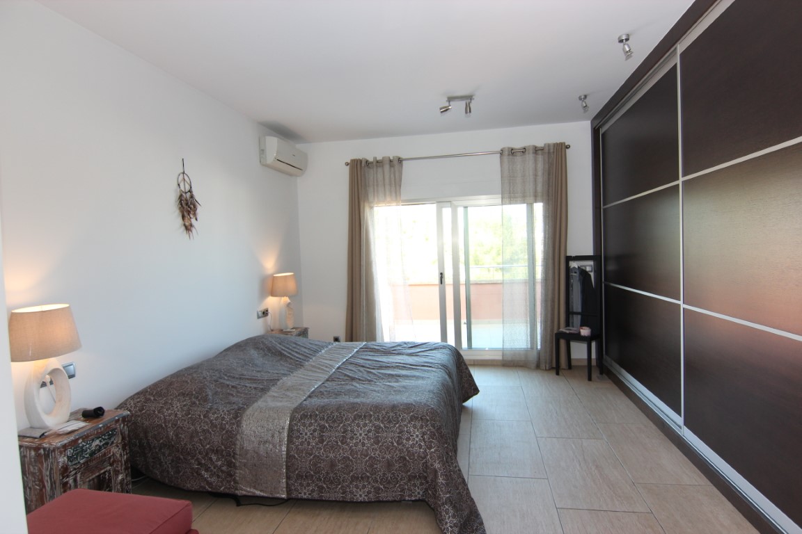 Dormitorio doble con amplio armario empotrado de puertas correderas oscuras, acceso directo a la terraza y suelos de gres porcelánico.