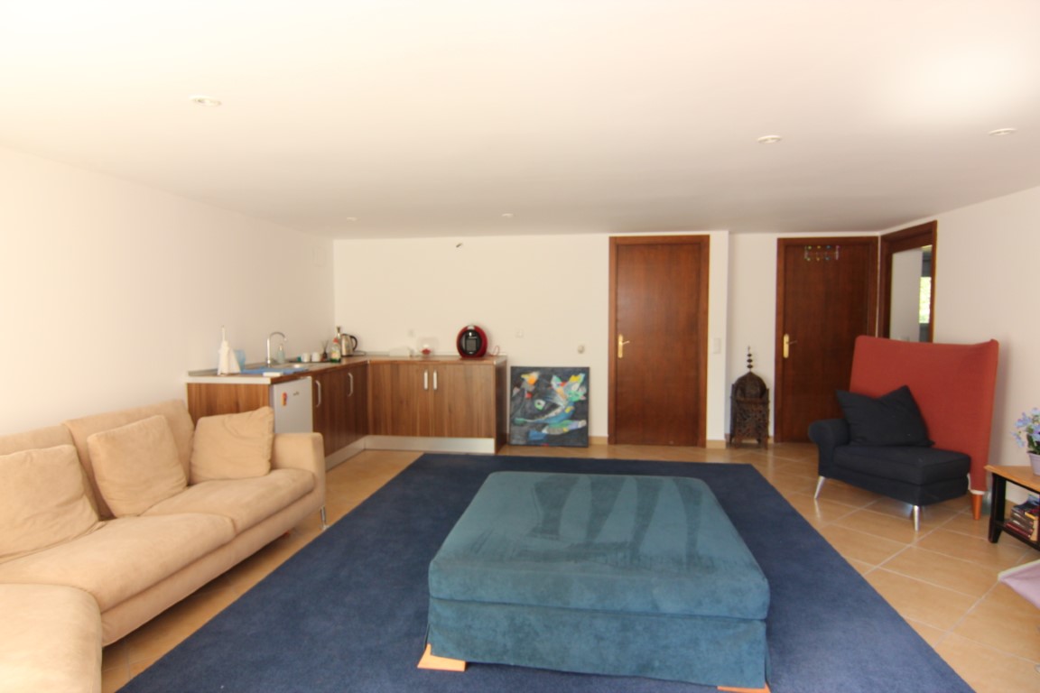 Salón del apartamento de invitados con cocina americana integrada, suelos cerámicos, iluminación empotrada y acceso a los dormitorios a través de puertas de madera.