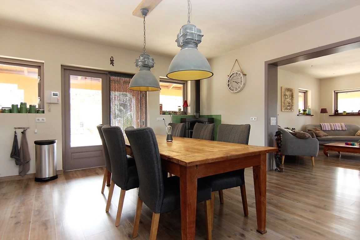 Comedor con mesa de madera maciza, sillas tapizadas en gris y lámparas de estilo industrial, integrado en un espacio abierto que conecta con el salón.